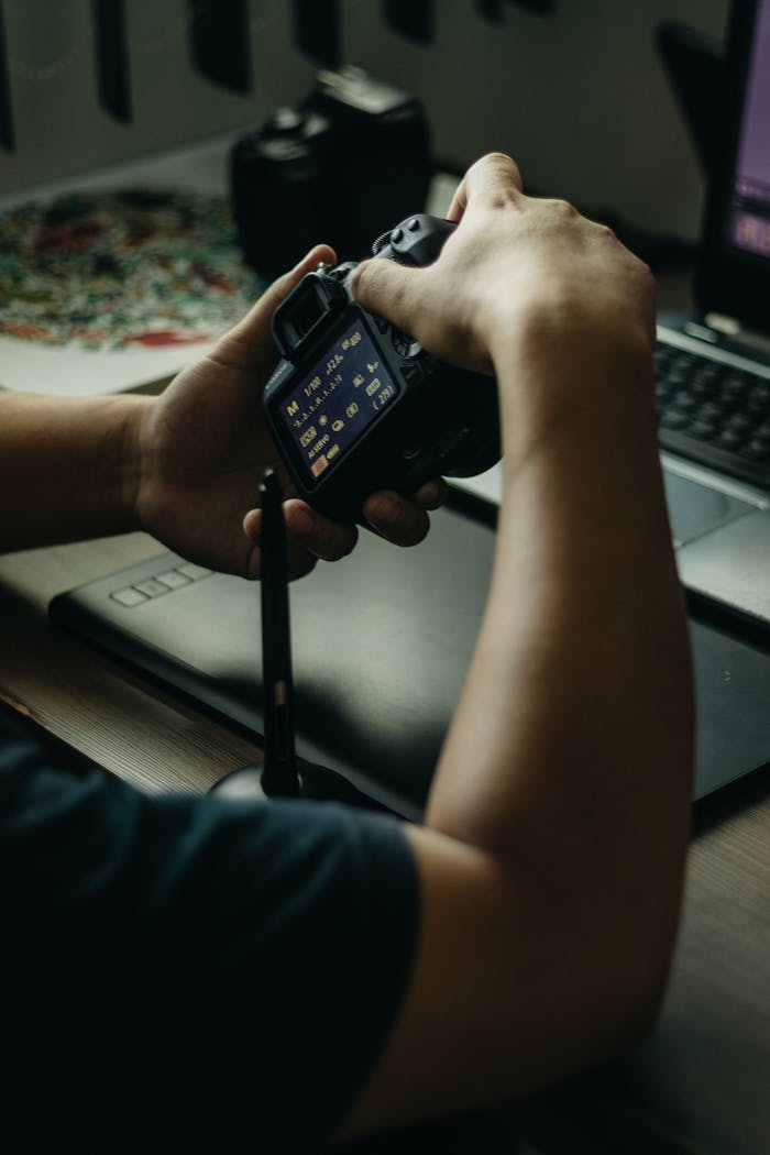 Person adjusting camera settings with editing tools nearby in creative workspace.