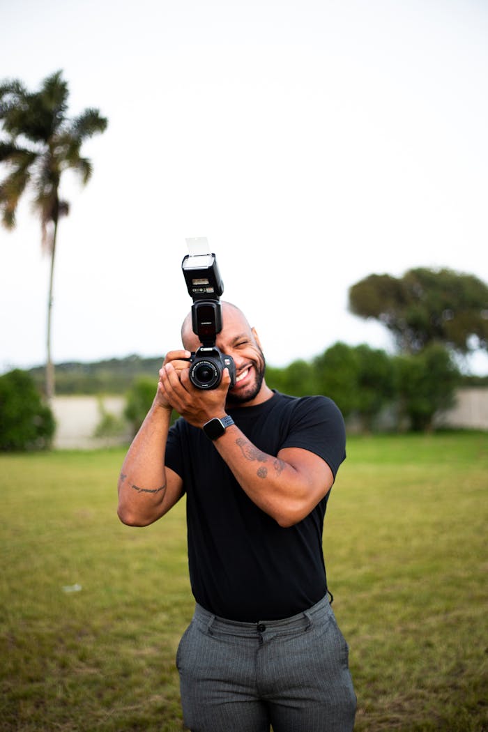 A cheerful photographer with a camera flashes a friendly smile outdoors.